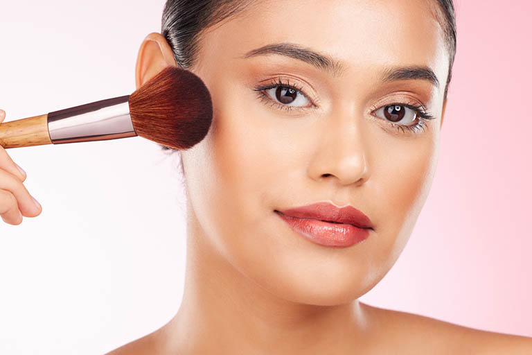 Beauty, makeup and portrait of woman in studio with a brush for cheek blush or foundation for glam routine. Cosmetics, face and young female model with cosmetology product isolated by pink background