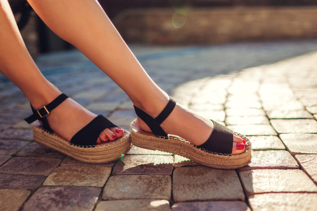 Stylish woman wearing black summer shoes with straw sole outdoors. Comfortable sandals.